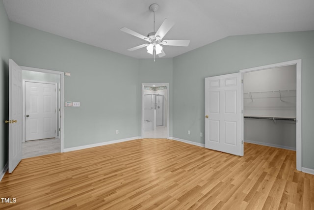 unfurnished bedroom with baseboards, a spacious closet, vaulted ceiling, light wood-style floors, and a closet