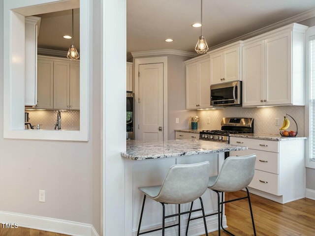 kitchen featuring a breakfast bar, hanging light fixtures, appliances with stainless steel finishes, light wood-style floors, and light stone countertops