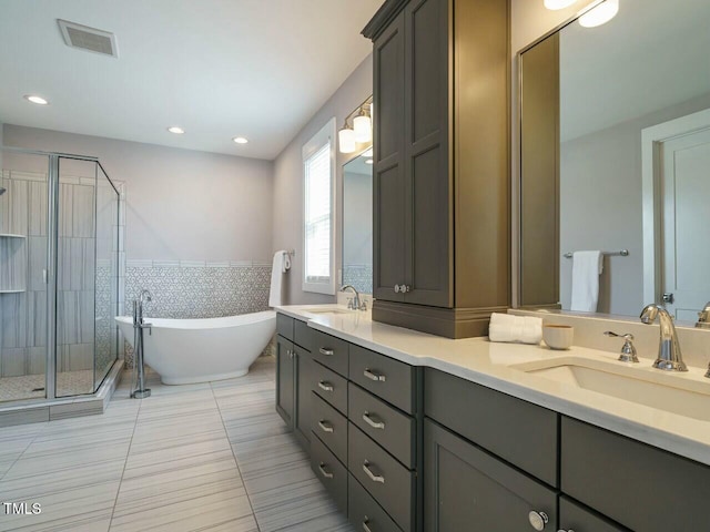 full bathroom featuring double vanity, visible vents, a sink, a shower stall, and a freestanding tub