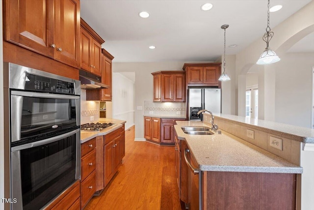 kitchen with tasteful backsplash, arched walkways, stainless steel appliances, under cabinet range hood, and a sink