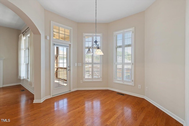 unfurnished dining area with arched walkways, wood finished floors, visible vents, and baseboards