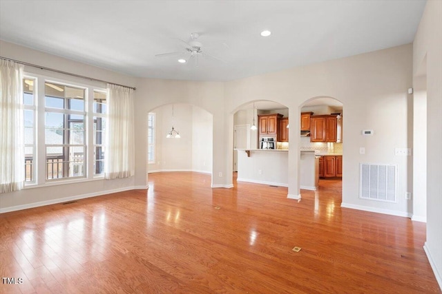 unfurnished living room with light wood-style floors, arched walkways, visible vents, and a ceiling fan