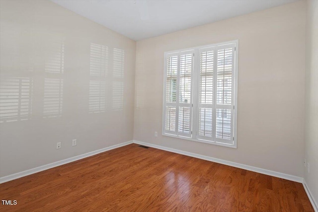 empty room featuring wood finished floors, visible vents, and baseboards