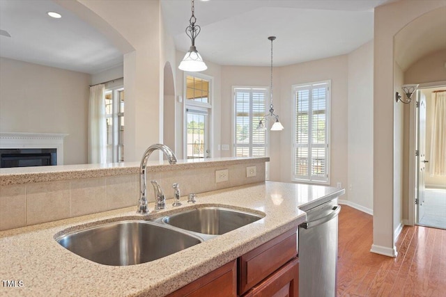 kitchen with brown cabinetry, a glass covered fireplace, a sink, light stone countertops, and dishwasher