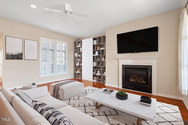 living area featuring baseboards, a glass covered fireplace, ceiling fan, wood finished floors, and recessed lighting