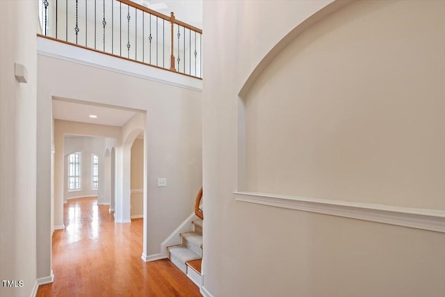 corridor with baseboards, arched walkways, a towering ceiling, wood finished floors, and stairs