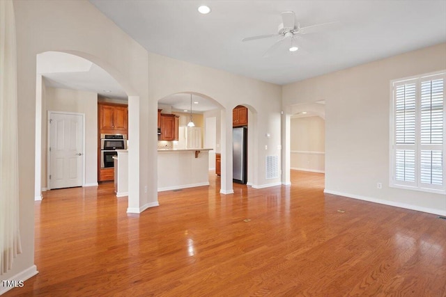 unfurnished living room with ceiling fan, arched walkways, recessed lighting, baseboards, and light wood finished floors