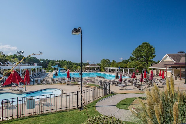 pool with a patio area, fence, and a water slide