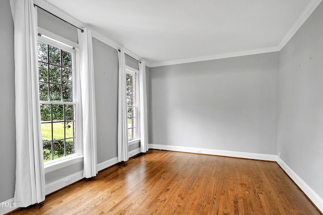 empty room with wood finished floors, baseboards, and ornamental molding