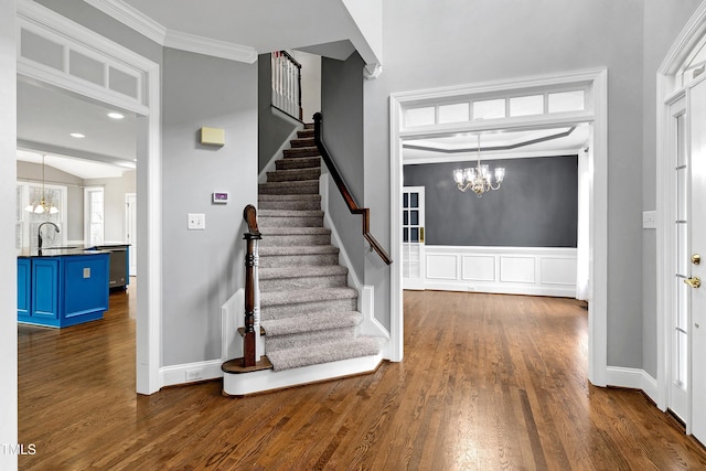 interior space with a chandelier, stairway, ornamental molding, wainscoting, and dark wood-style flooring