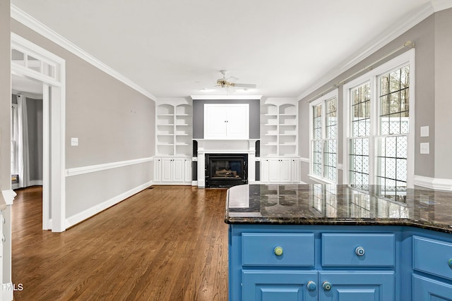 kitchen featuring a fireplace with flush hearth, ornamental molding, blue cabinetry, dark wood finished floors, and baseboards