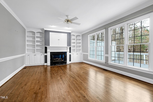 unfurnished living room featuring a fireplace with flush hearth, built in features, crown molding, baseboards, and dark wood-style flooring