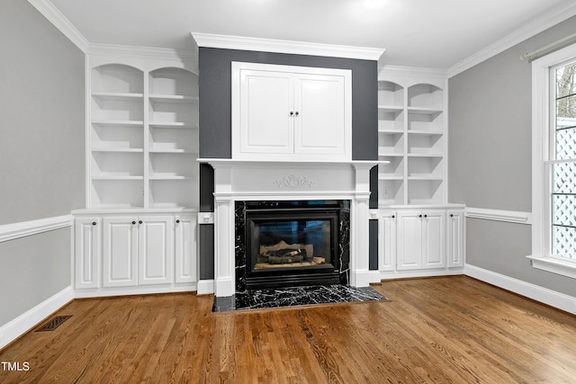 unfurnished living room with built in features, visible vents, a fireplace with flush hearth, and wood finished floors