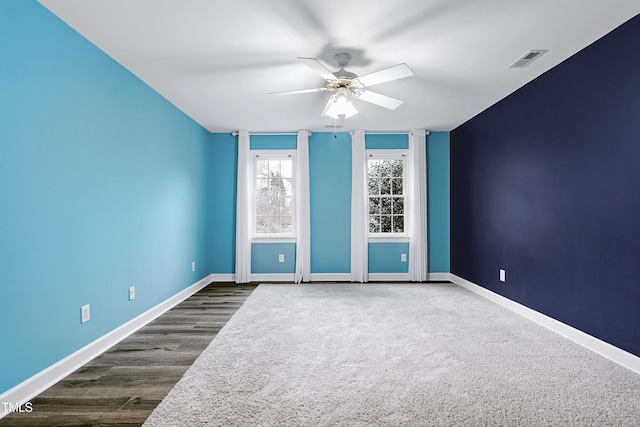 empty room featuring visible vents, baseboards, dark wood-style flooring, and a ceiling fan