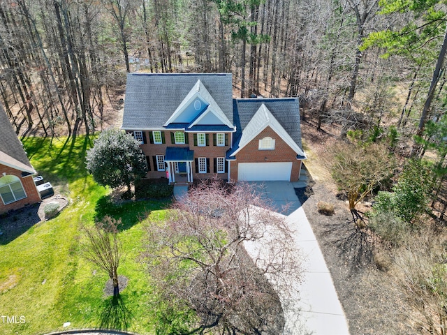 view of front of home featuring a front yard, a forest view, an attached garage, concrete driveway, and brick siding