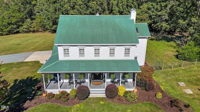 view of front of house with covered porch, metal roof, a front lawn, and a chimney