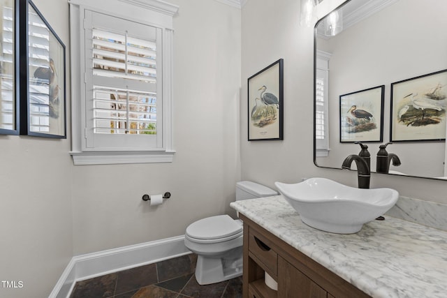 half bathroom featuring toilet, stone finish floor, baseboards, and vanity