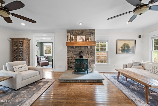 living area with baseboards, a ceiling fan, wood finished floors, a wood stove, and crown molding