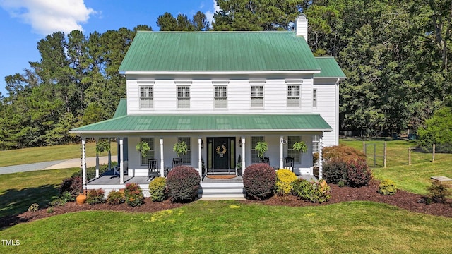 view of front of property featuring covered porch, a chimney, metal roof, and a front yard