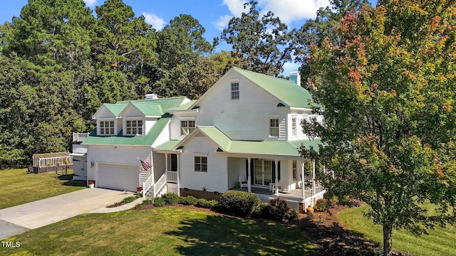 view of front of home with metal roof, covered porch, a garage, concrete driveway, and a front yard