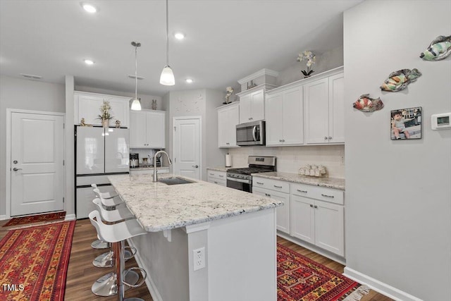 kitchen featuring a breakfast bar area, stainless steel appliances, white cabinets, a sink, and an island with sink