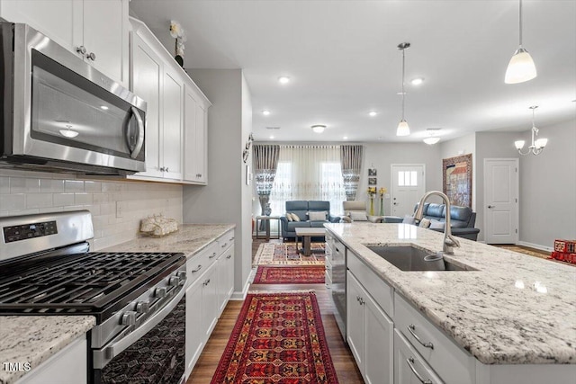 kitchen featuring a kitchen island with sink, stainless steel appliances, a sink, white cabinetry, and open floor plan