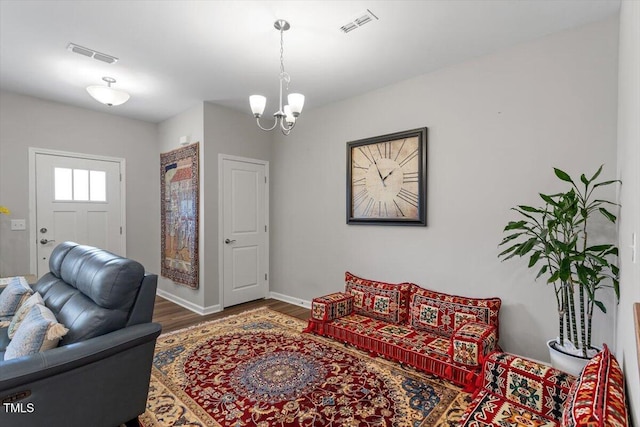 living area with baseboards, visible vents, an inviting chandelier, and wood finished floors