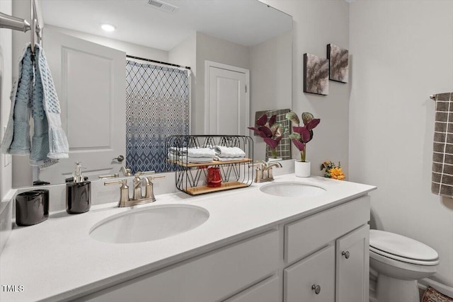 bathroom featuring toilet, double vanity, a sink, and visible vents