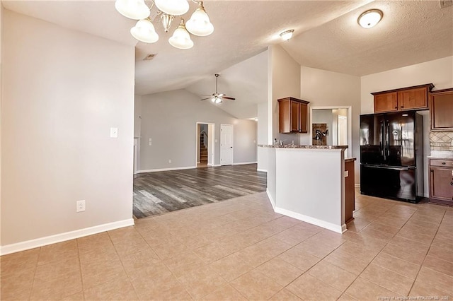 kitchen featuring lofted ceiling, visible vents, freestanding refrigerator, dark stone counters, and ceiling fan with notable chandelier