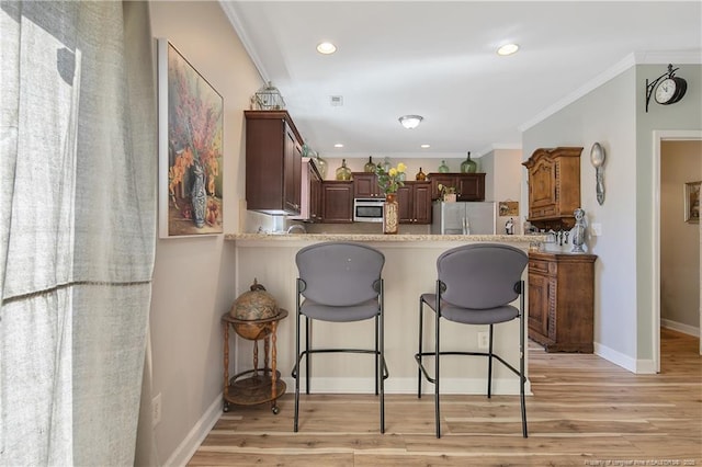 kitchen with appliances with stainless steel finishes, crown molding, light wood finished floors, and a kitchen bar