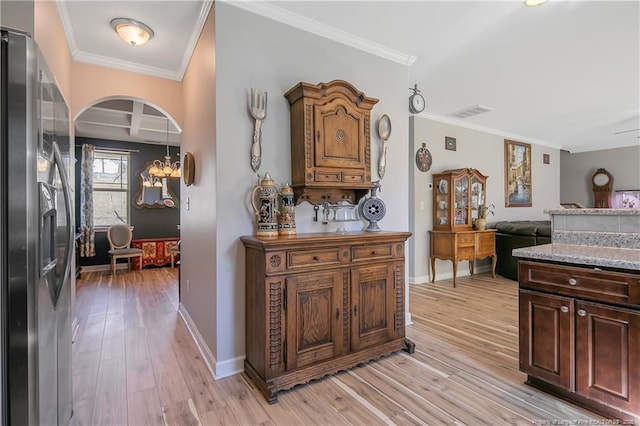 interior space featuring baseboards, ornamental molding, arched walkways, and light wood-style floors