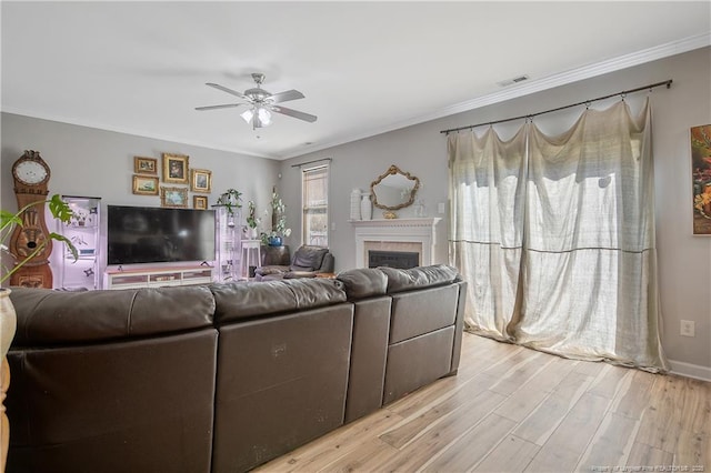 living room featuring a fireplace, light wood finished floors, visible vents, ornamental molding, and a ceiling fan