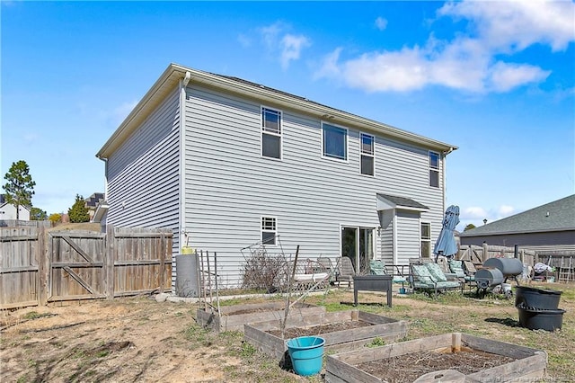 rear view of property with heating fuel, a garden, a gate, and fence