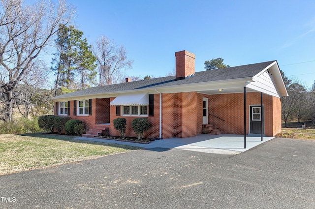 single story home with entry steps, a chimney, an attached carport, and brick siding