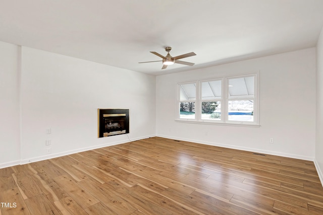 unfurnished living room with a ceiling fan, baseboards, a fireplace, and light wood finished floors