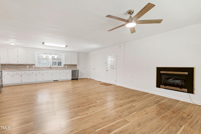 unfurnished living room with a fireplace, a sink, a ceiling fan, baseboards, and light wood-style floors