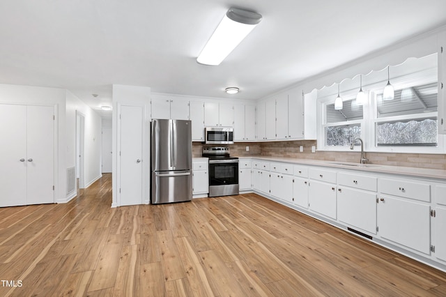 kitchen featuring light countertops, backsplash, appliances with stainless steel finishes, light wood-style floors, and a sink