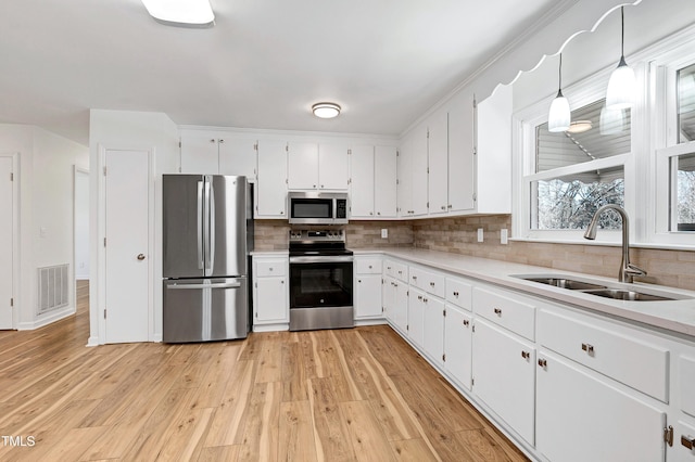 kitchen with stainless steel appliances, a sink, white cabinetry, visible vents, and light wood-style floors