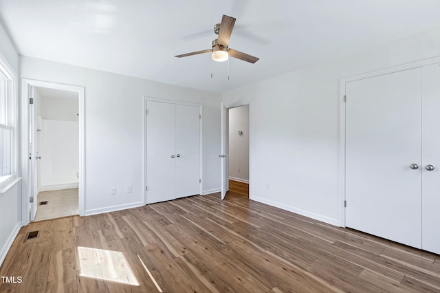 unfurnished bedroom with ensuite bath, wood finished floors, visible vents, and baseboards