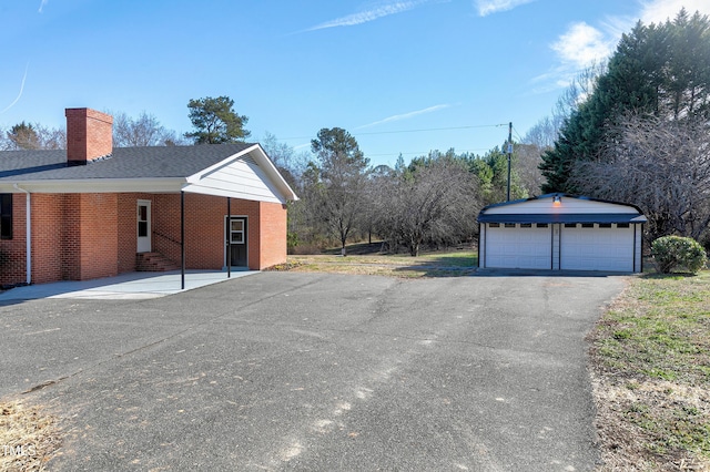 exterior space with an outbuilding, brick siding, a detached garage, roof with shingles, and a chimney