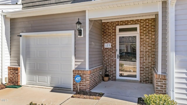 doorway to property with a garage and brick siding