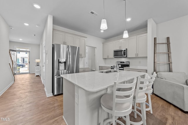 kitchen featuring pendant lighting, appliances with stainless steel finishes, light wood-style floors, a sink, and a kitchen breakfast bar