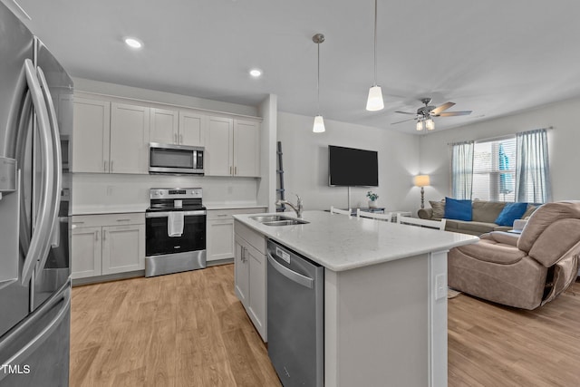 kitchen with light wood-style floors, appliances with stainless steel finishes, open floor plan, and a sink