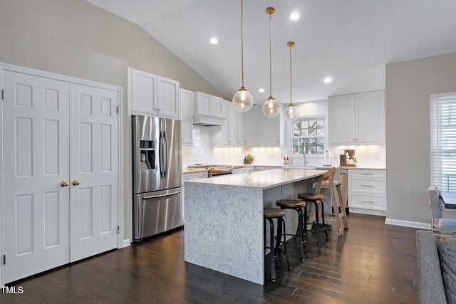 kitchen with dark wood-style floors, vaulted ceiling, appliances with stainless steel finishes, a kitchen breakfast bar, and a center island