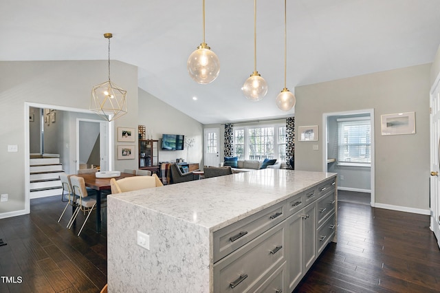 kitchen with dark wood-type flooring, pendant lighting, light stone counters, a kitchen island, and baseboards