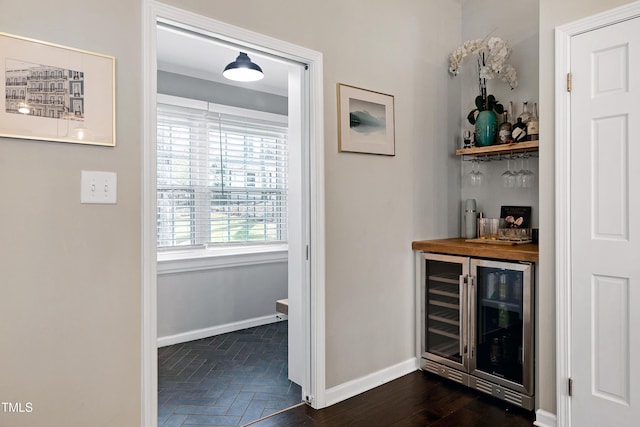 bar with parquet floors, baseboards, a bar, and beverage cooler