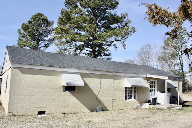 back of property featuring a shingled roof and concrete block siding