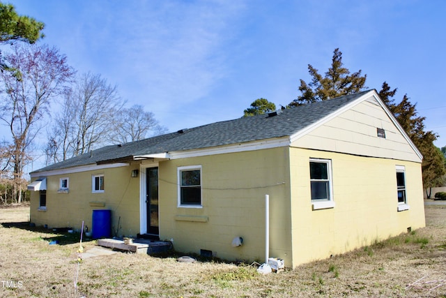 back of house featuring a shingled roof and concrete block siding