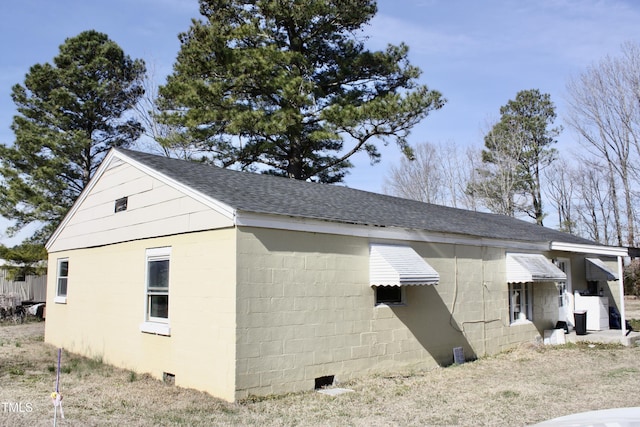 view of side of home featuring a shingled roof, concrete block siding, and crawl space