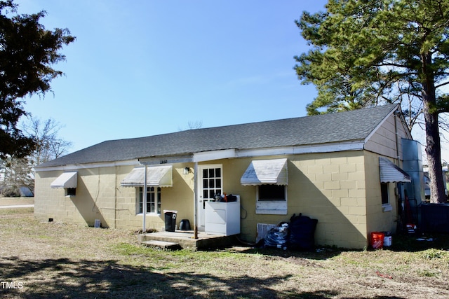 back of house featuring a shingled roof and concrete block siding